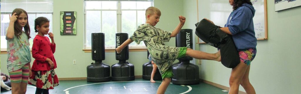 a boy kicking a bag held by counselor while two girls wait their turn