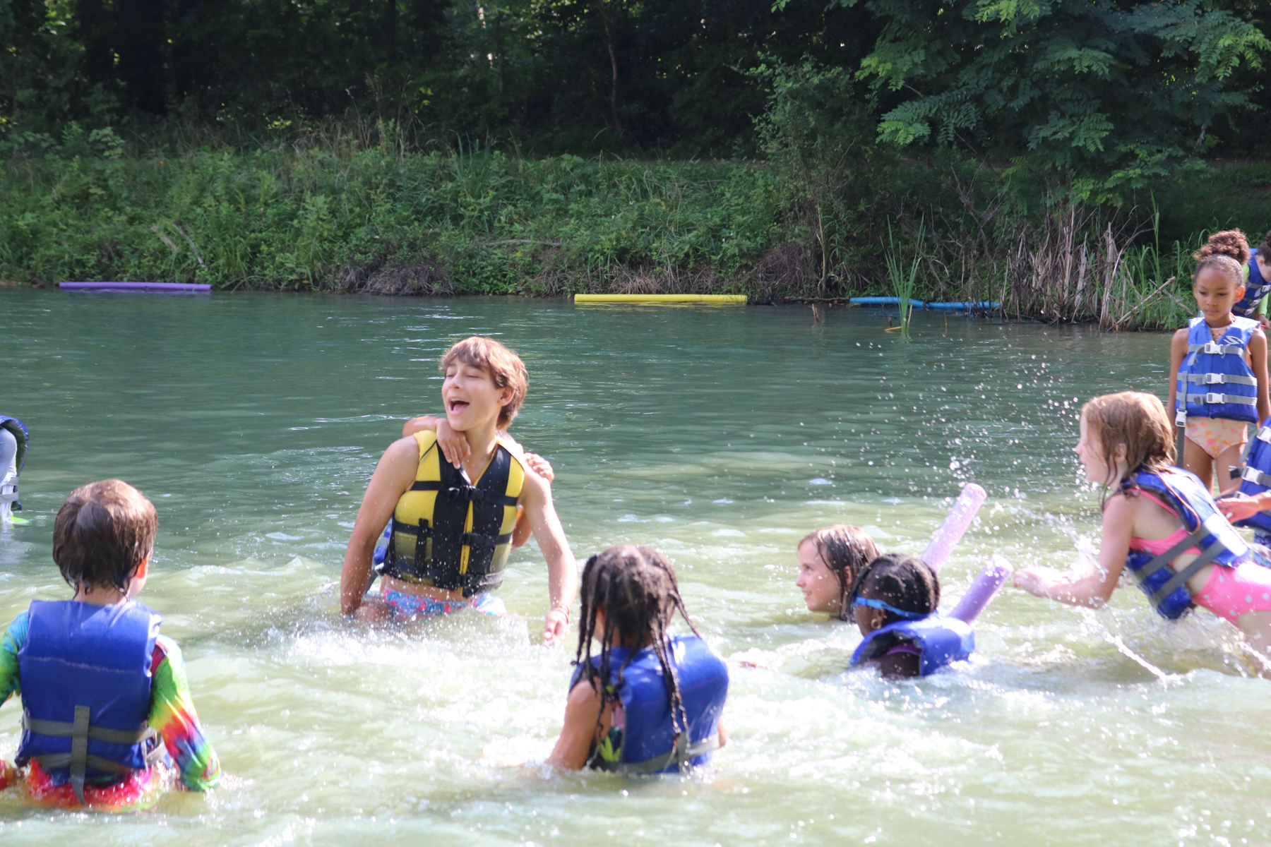 children in the pond playing with a male staff